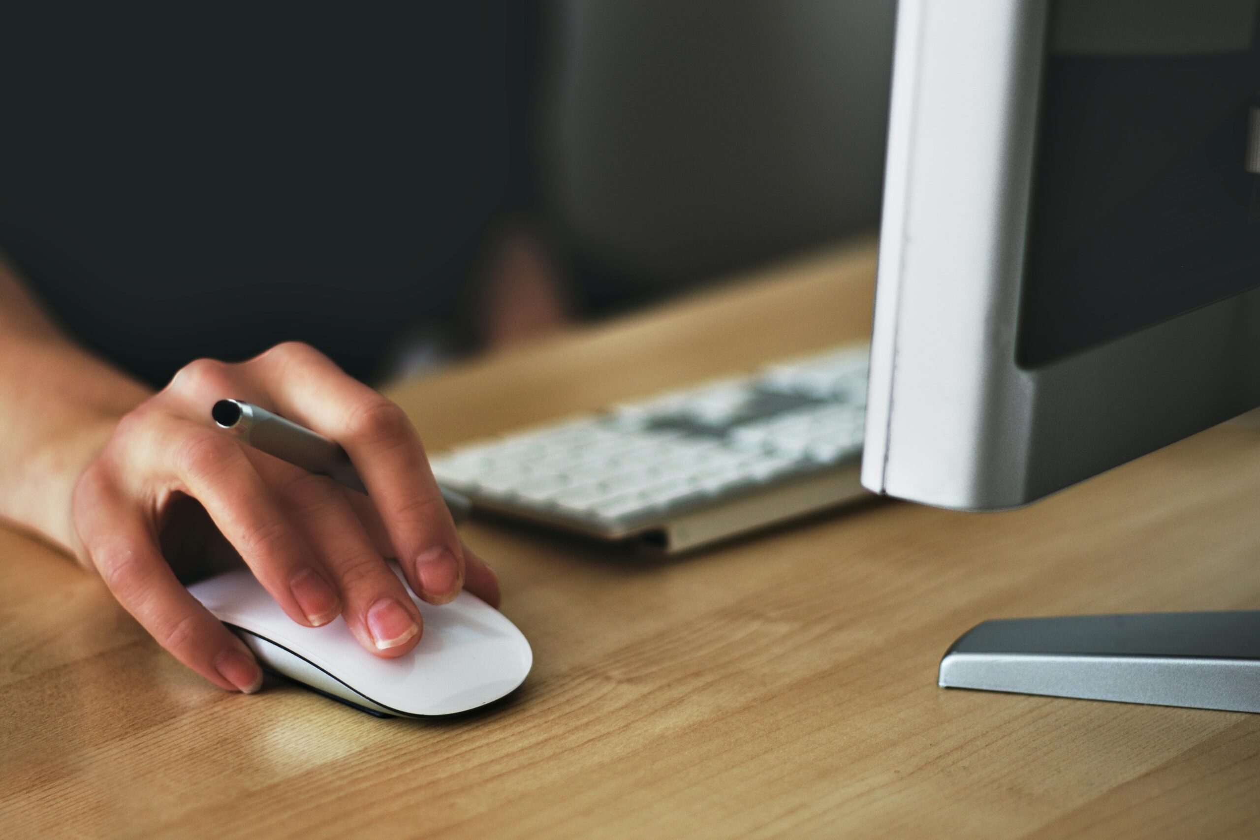 woman's hand using the mouse at her desk next to a computer